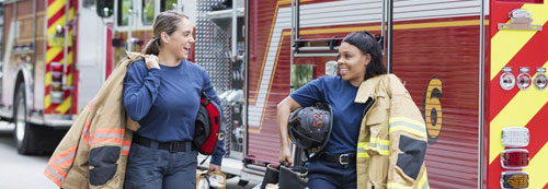 Two female firefighters walking next to fire trucks